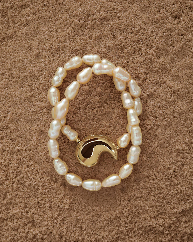 18K Gold Hero Spiral pendant and 18K Gold Peach freshwater pearl on a sand