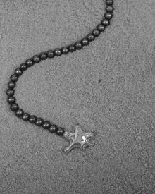 18K Gold Hero Water pendant and 18K Gold Midnight freshwater pearl on a sand