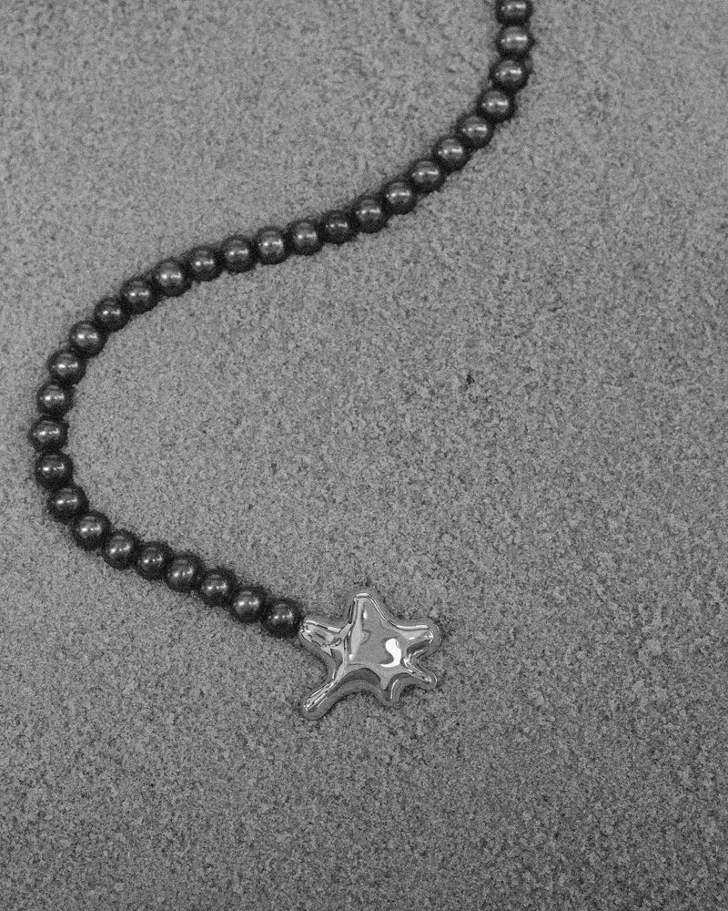 18K Gold Hero Water pendant and 18K Gold Midnight freshwater pearl on a sand
