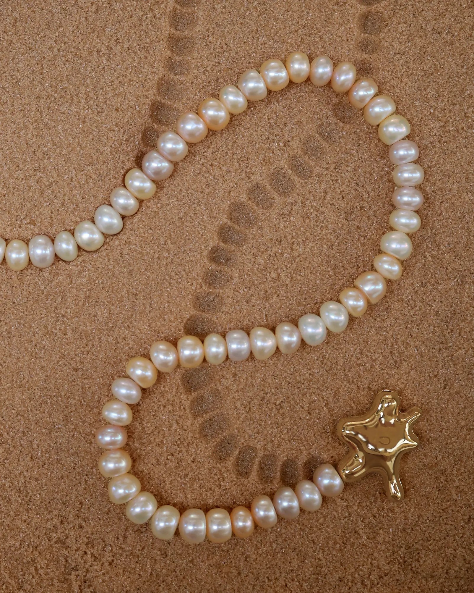 18K Gold Hero Water pendant and 18K Gold Freshwater pearl in Blush on a sand