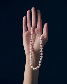 18K gold ivory pearl and red knots necklace draped over a hand against a black background