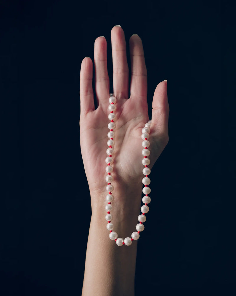 18K gold ivory pearl and red knots necklace draped over a hand against a black background