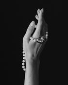 18K gold ivory pearl and red knots necklace and 18K gold heart-shaped pendant draped over a hand against a black background