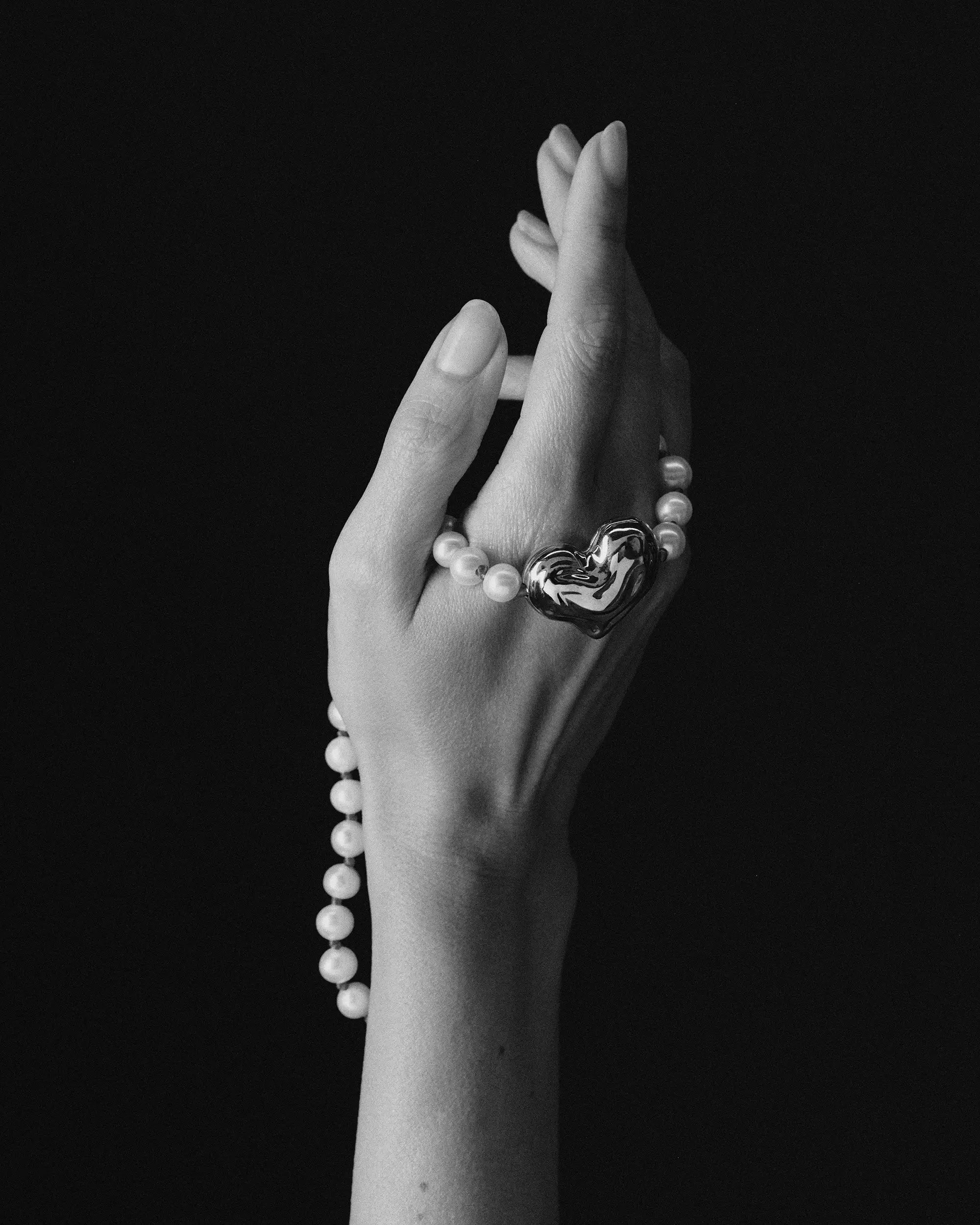 18K gold ivory pearl and red knots necklace and 18K gold heart-shaped pendant draped over a hand against a black background