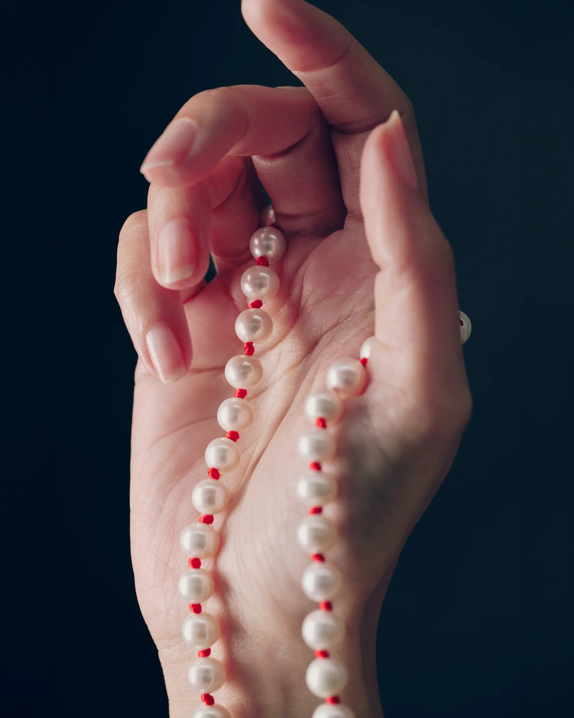 18K gold ivory pearl and red knots necklace draped over a hand against a black background