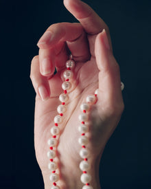 18K gold ivory pearl and red knots necklace draped over a hand against a black background