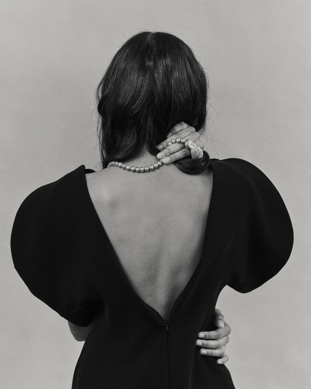 Black and white photo of a model wearing an open-back dress with 18K gold pearl necklace.
