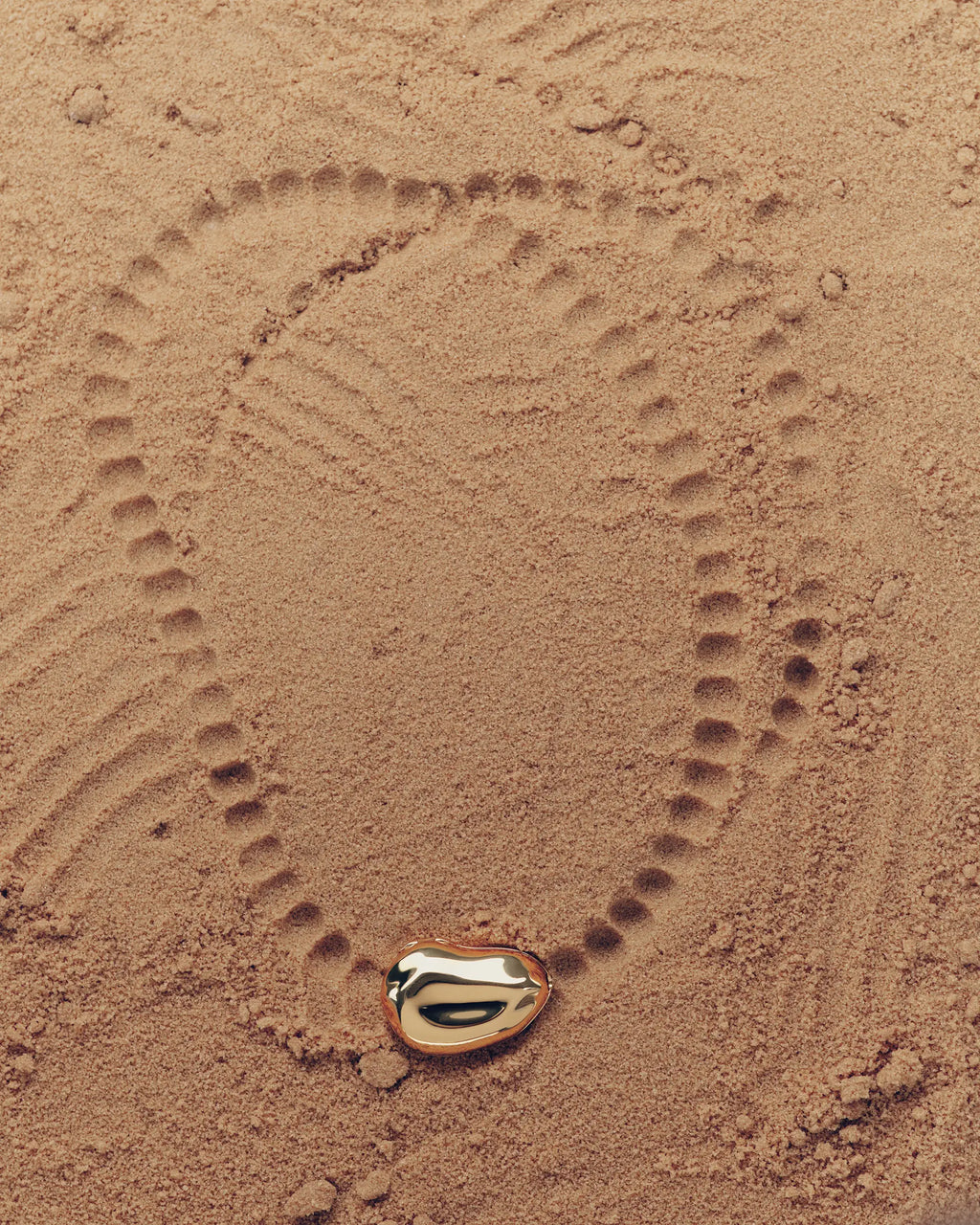18K gold pomegranate-shaped pendant on a sand